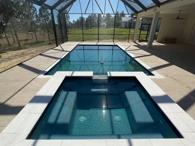 Rectangular swimming pool with attached hot tub in a glass encolsure